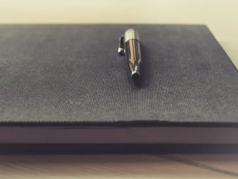 A silver pen resting on a closed grey notebook, ready to sign